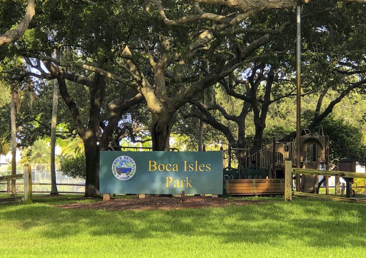 Boca Isles Park sign beneath the live oaks, with the playground behind